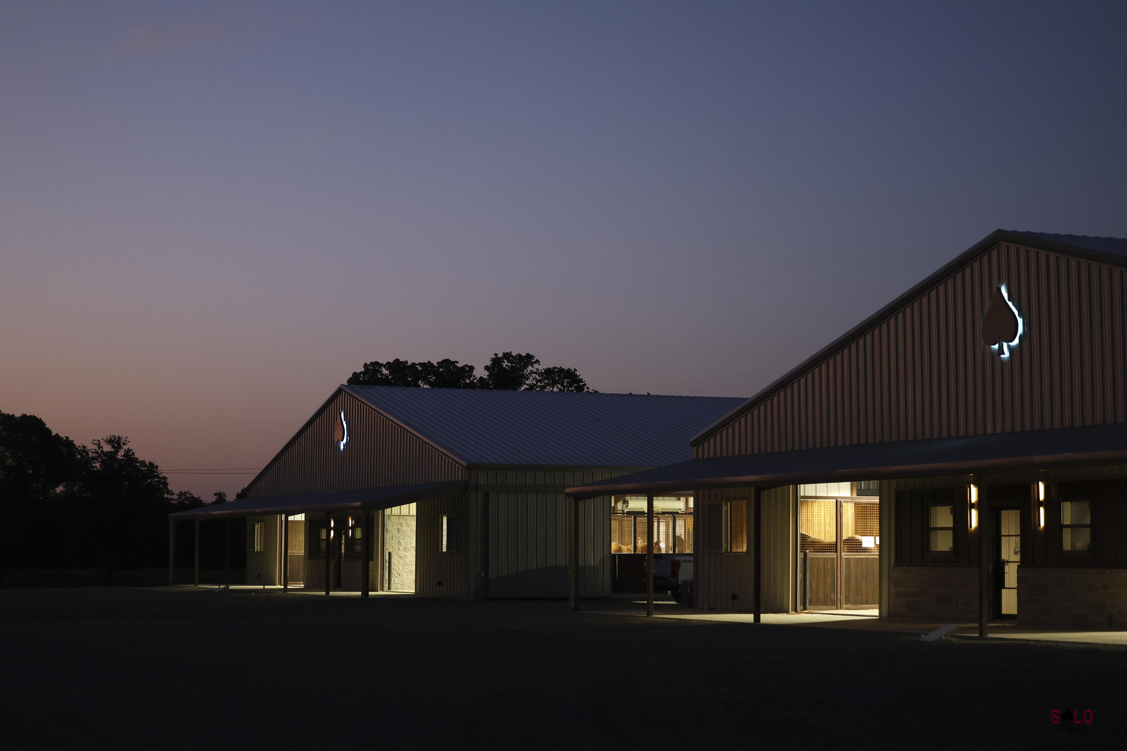 The barns at dusk, spade emblems lit on the gables