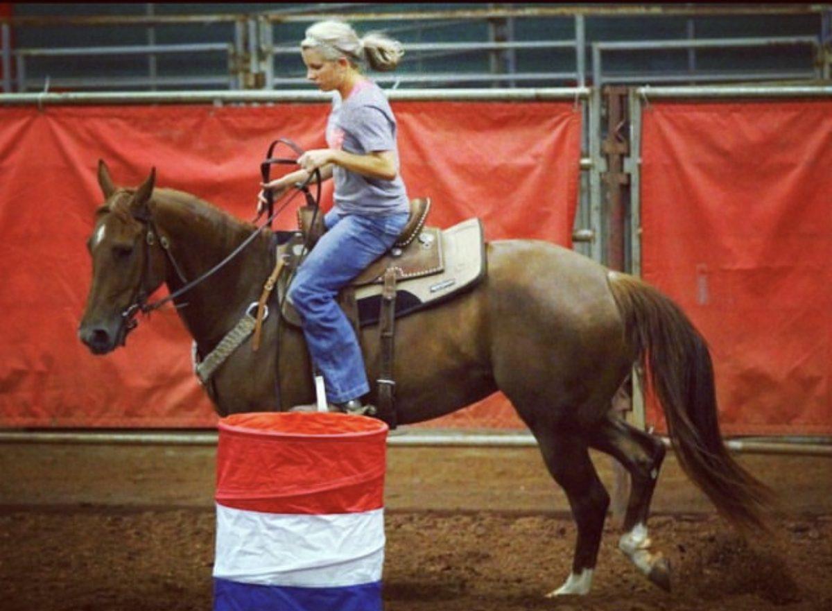Melanie loping a young horse past a barrel in the practice pen