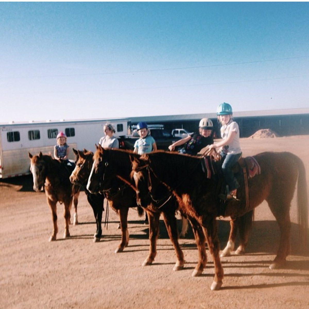 Five lesson girls lined up horseback after a trail ride