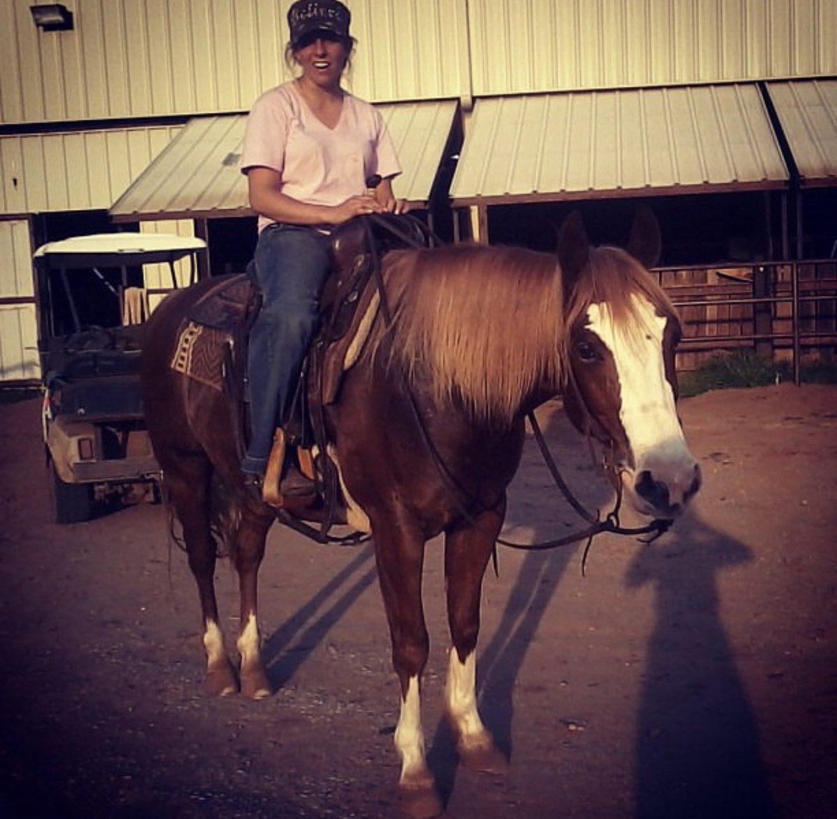 A young Melanie Smith horseback outside a barn